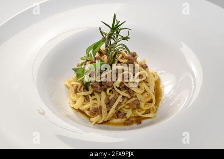 Fettuccine alla Bolognese, Tagliolini-Pasta mit Fleischsoße und Salbei- und Majoran-Zweige in einem weißen Gericht Stockfoto