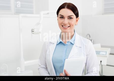 Porträt eines lächelnden Zahnarztes, der Tablet hält und die Kamera anschaut In der Zahnklinik Stockfoto