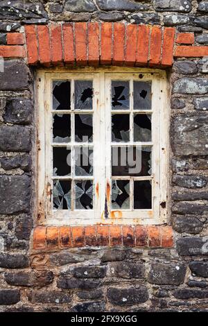 Altes Schiebefenster, mit zerbrochenem Glas und einem Graffiti des Witzboldes im Hintergrund Stockfoto