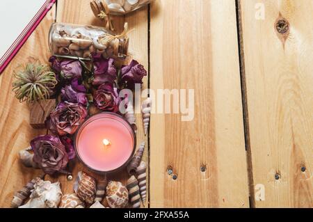 Bild eines Holztisches, der mit einer rosa Kerze, Muscheln und getrockneten Rosen geschmückt ist. Stockfoto