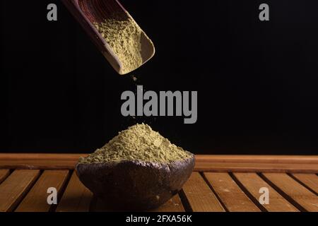 matcha, grüner Tee in Tontopf und ein Holzspatel streut Tee auf Holzhintergrund. Food Photography Stockfoto