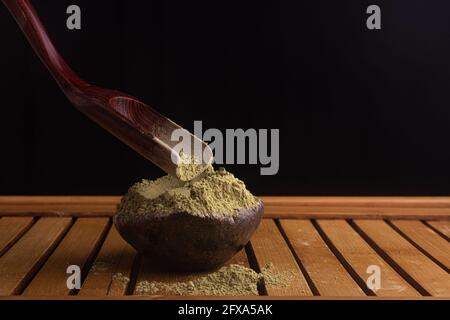 matcha, grüner Tee in Tontopf und ein Holzspatel streut Tee auf Holzhintergrund. Food Photography Stockfoto