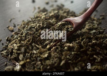 Grüner Tee und ein Holzspatel streut Tee auf hölzernen Hintergrund. Food-Fotografie Stockfoto