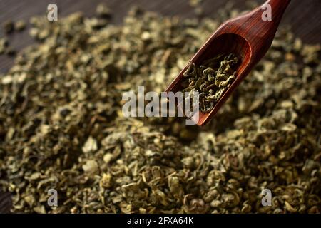 Grüner Tee und ein Holzspatel streut Tee auf hölzernen Hintergrund. Food-Fotografie Stockfoto