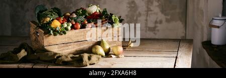 Breite Winkel der Holzkiste mit verschiedenen reifen Früchten und Gemüse auf dem Tisch im rustikalen Raum platziert Stockfoto