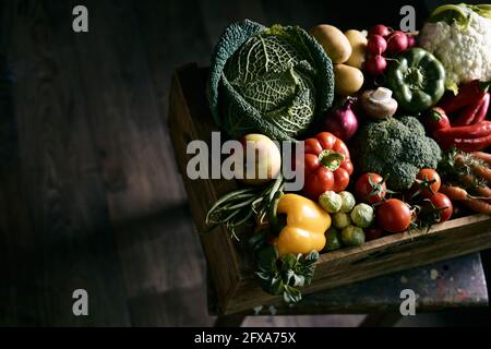 Von oben Kasten mit verschiedenen frischen Gemüse auf Stuhl gelegt Über dunklem Boden in rustikalem Zimmer Stockfoto