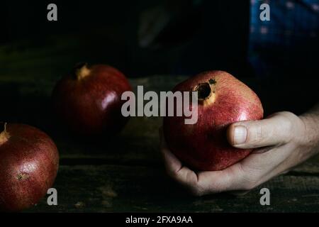 Hoher Winkel von anonymen Männchen zeigt frischen Granatapfel über rustikal Tisch im dunklen Raum Stockfoto