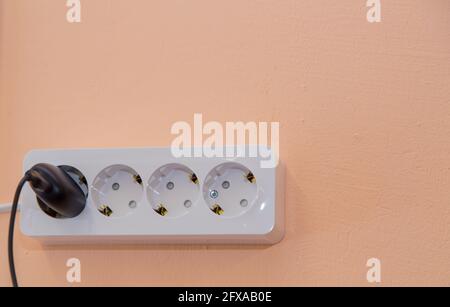 Eine Steckdose mit einem schwarzen Stecker, der an einer beigefarbenen Wand eingeklebt ist. Elektrische weiße Elemente werden horizontal an der Wand montiert. Es ist Speicherplatz für Kopien vorhanden. Stockfoto