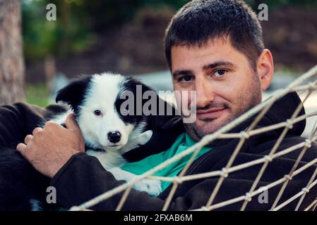 Kaukasischer Mann kuschelt Border Collie Welpe in einer Hängematte Zweisamkeit Und Liebe Stockfoto