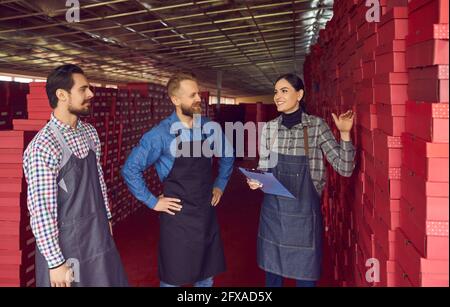 Glückliche Arbeiter, die im Gang zwischen den Kisten stehen Im Schuhfabriklager Stockfoto