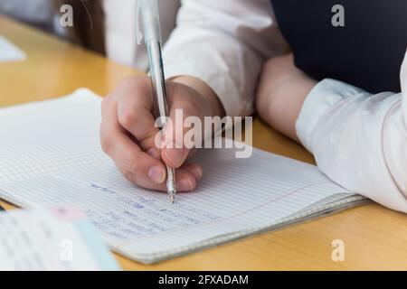 Eine Mädchenhand mit einem Kugelschreiber in Nahaufnahme schreibt in einer schönen Handschrift. Der Studierende schließt die Aufgabe ab. Ein Student löst an einem Schreibtisch in der Schule Beispiele in Mathematik. Warmes, weiches Tageslicht. Stockfoto