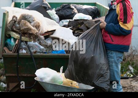 Ein junger Mann wirft einen großen Plastikmüllbeutel in den Müllcontainer draußen Stockfoto