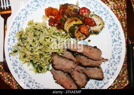 Nahaufnahme einer Portion toskanisches Steak mit Orzo, gebratenen Zucchini und Kirschtomaten. Stockfoto