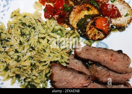 Nahaufnahme einer Portion toskanisches Steak mit Orzo, gebratenen Zucchini und Kirschtomaten. Stockfoto