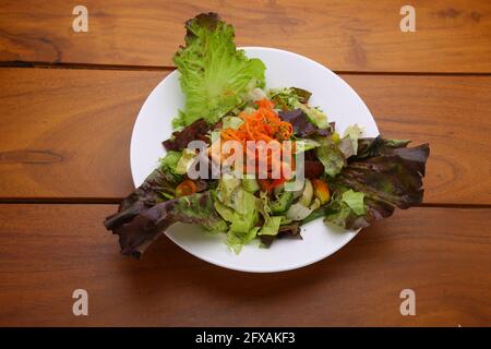 Grüner Salat mit dunklem Blattgrün, gesunder Salat mit Blattgrün, wunderschön angerichtet Eine weiße Platte mit Holzhintergrund Stockfoto