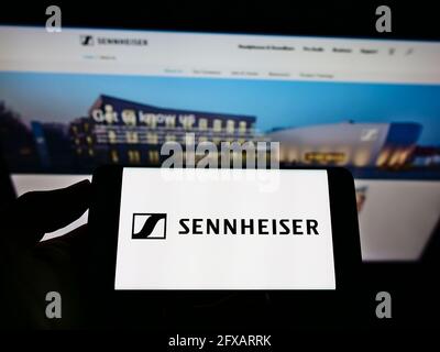 Person, die das Mobiltelefon mit dem Logo des deutschen Audiounternehmens Sennheiser electronic GmbH Co KG auf dem Bildschirm vor der Webseite hält. Konzentrieren Sie sich auf die Telefonanzeige. Stockfoto