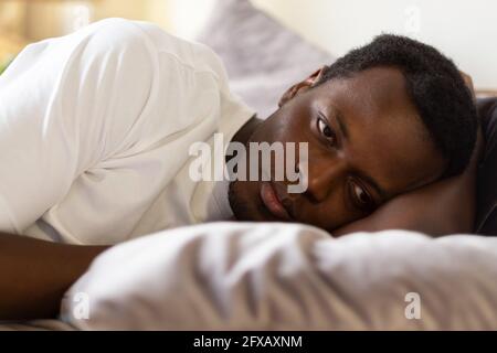 Afrikanischer müder Mann kann nicht von Schlaflosigkeit schlafen Stockfoto