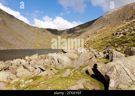 Felsen und Geröll von Goat's Water in Cumbria, England. Dow Crag erhebt sich über dem See im Lake District National Park. Stockfoto