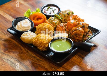 tandoori gebraten gebratenen Momos dimsum pakora mit Gemüseblümchen und grünen, weißen und roten Sauce in einem schwarzen Teller auf einem Holztisch gelegt Stockfoto