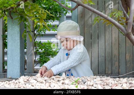 Baby Girl Sammelt Steine Im Garten. Kreative Outdoor-Aktivitäten für Kinder Stockfoto