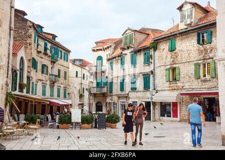 SPLIT, KROATIEN - 10. OKTOBER 2014: Touristen, die auf dem Platz Trg Brace Radic mit alten mittelalterlichen Häusern im Hintergrund spazieren gehen. Split ist eine große Tour Stockfoto