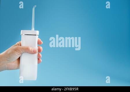 Irrigator in der Hand zum Reinigen des Mundes auf blauem Hintergrund. Ein mobiles Gerät zum Zähneputzen und einem schneeweißen Lächeln. Freier Speicherplatz Stockfoto