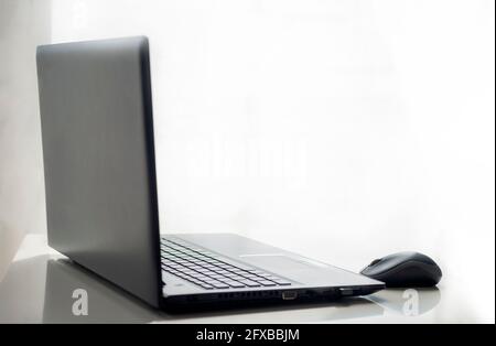Schwarzer Laptop und kabellose Maus auf einem weißen Tisch mit weißem Hintergrund. Objekt- und Lifestyle-Konzept Stockfoto