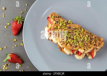 Sandwich-Waffeln mit Banane, Erdbeere und Schokolade und Pistazie auf der Oberseite Stockfoto