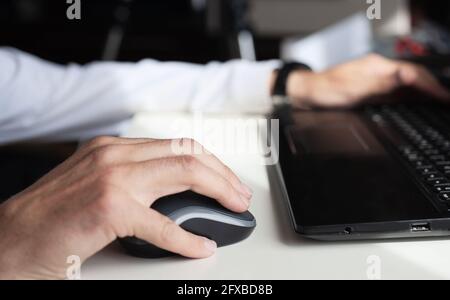 Nahaufnahme der Hände eines Mannes, der mit einem Laptop und arbeitet Eine Maus Stockfoto