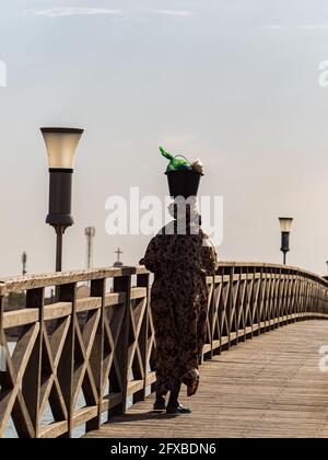 Joal-Fadiouth, Afrika - Jan, 2019: Senegalesische Frau mit einem Eimer auf dem Kopf auf einer Holzbrücke zwischen Joal und Fadiouth. Die Region Thiès am en Stockfoto