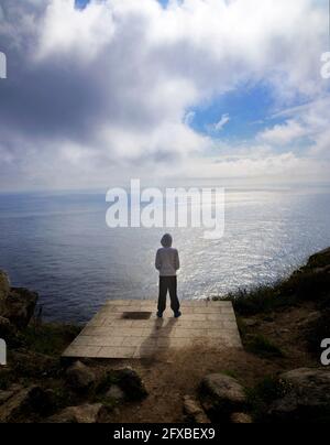 Junger Mann von hinten, der den Horizont auf dem sieht Rand einer Klippe mit dem Himmel und dem Meer Im Hintergrund Stockfoto