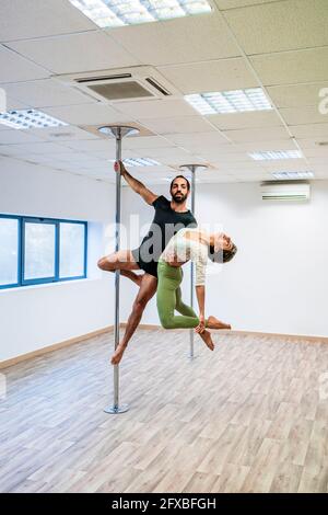 Männlicher akrobaten, der eine Tänzerin trägt, während er im Tanzstudio an der Stange hängt Stockfoto