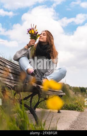 Junge Frau riecht Blumen auf der Bank in der Natur Stockfoto