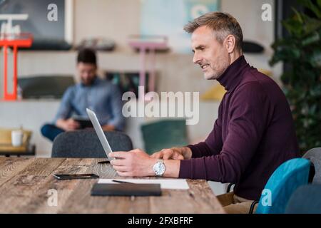 Männlicher Profi, der am Arbeitsplatz am Laptop über dem Tisch arbeitet Stockfoto