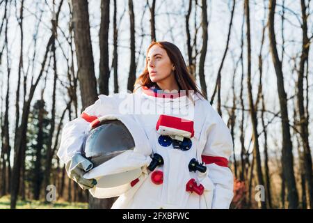 Nachdenkliche Astronautin mit Weltraumhelm, die im Wald wegschaut Stockfoto