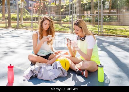 Frauen, die Mobiltelefone benutzen, während sie auf dem Hof im Park sitzen Stockfoto
