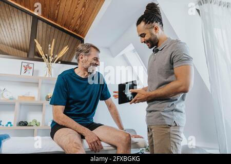 Physiotherapeut diskutiert in der Praxis digitales Röntgenbild des Knies mit einem männlichen Patienten Stockfoto