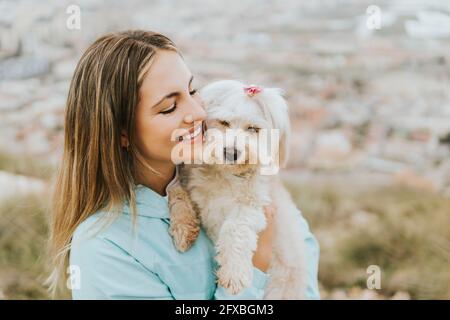 Schöne Frau lächelt, während sie Hund umarmt Stockfoto