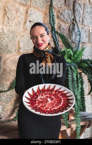 Lächelnde Besitzerin mit Teller mit rotem Fleisch im Restaurant Stockfoto