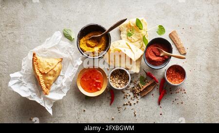 Studioaufnahme von Samosa-Knödel auf Papierservietten, Masala-Gewürzen, Chili-Dipping-Sauce, Naan-Brot und roten Chilischoten Stockfoto