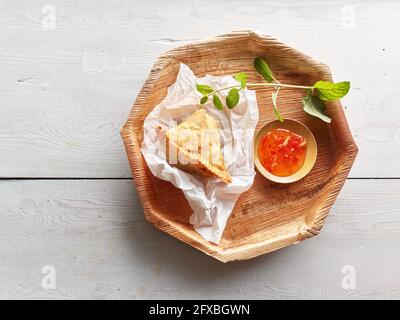 Studioaufnahme eines hölzernen Untersetzer mit Samosa-Knödel und Schüssel mit Chilisauce Stockfoto