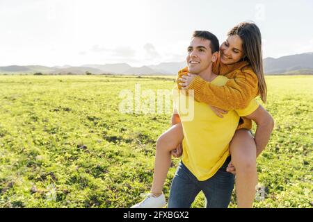 Freund Huckepack Freundin auf Wiese während sonnigen Tag Stockfoto