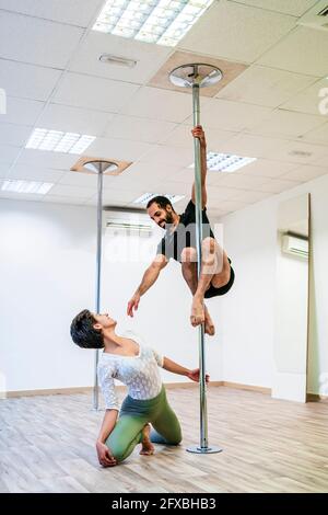 Weibliche Tänzerin, die im Tanzstudio einen männlichen akrobaten beim Üben auf der Stange ansieht Stockfoto