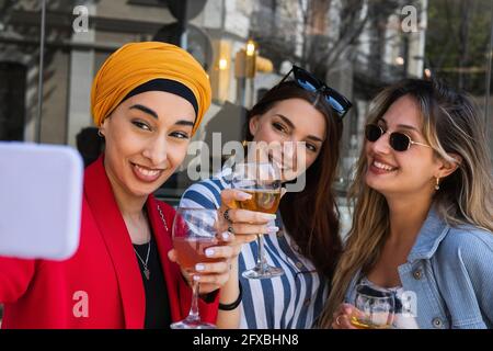 Junge Frau nimmt Selfie mit weiblichen Freunden, während sie trinkt Stockfoto