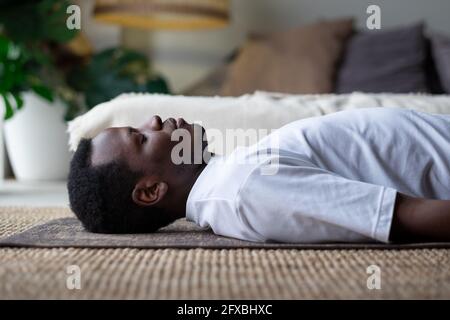 Yoga. Afrikanischer junger Mann, der auf einem Boden meditiert und in Shavasana-Pose liegt. Stockfoto