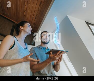 Physiotherapeutin und Patientin mit Blick auf holographisches anatomisches Modell der Wirbelsäule Stockfoto