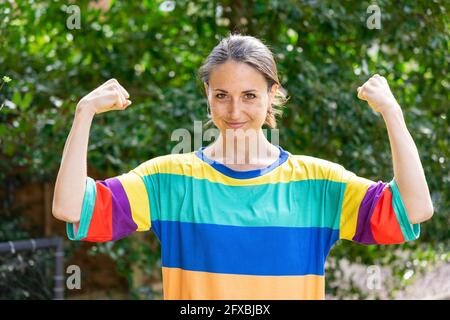 Schöne Frau mittleren Erwachsenen trägt mehrfarbige oben Biegegefühl Bizeps im Garten Stockfoto