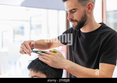 Männlicher Barbier, der im Salon die Haare eines Jungen im Teenageralter schneidet Stockfoto