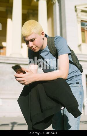 Teenager im Rucksack und Sweatshirt, der sich auf einem Skateboard stützt und tippt Auf seinem Handy Stockfoto