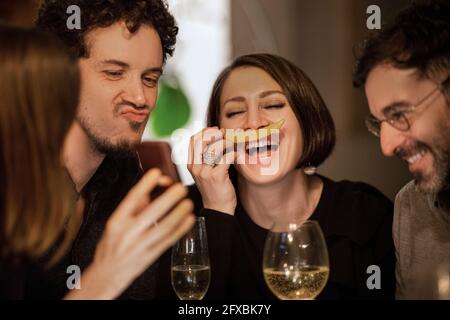 Reife Frau, die zu Hause fröhliche männliche und weibliche Freunde mit ihrem Mobiltelefon beschwing Stockfoto